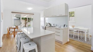 Une cuisine moderne avec des meubles blancs, un îlot central et un coin repas avec des chaises blanches.