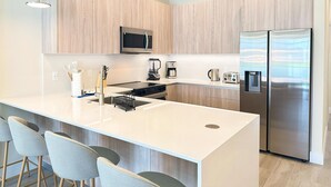 Eine moderne Küche mit Holzschränken, Edelstahlgeräten, einer zentralen Kochinsel mit Barhocker und Pendelleuchten.