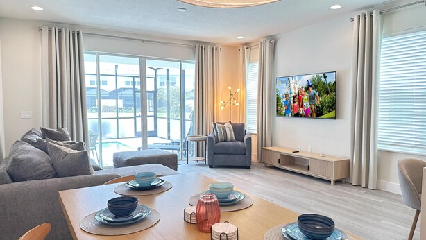Ein modernes Wohnzimmer mit Essbereich, großen Fenstern und einem flachbildfernseher an der Wand.