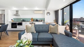 Un salon moderne avec un canapé gris, un coin repas, une cuisine et un balcon offrant une vue agréable.