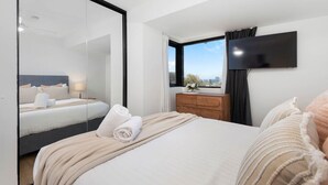 Une chambre d’hôtel dotée d’un grand lit, d’un téléviseur à écran plat fixé au mur, d’une commode en bois et d’une fenêtre donnant sur la ville.