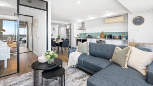 Un salon moderne avec un canapé gris, une table basse et, au fond, un coin repas.