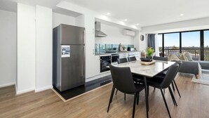 Une cuisine moderne dotée d’un réfrigérateur en acier inoxydable, un coin repas avec une table en marbre et des chaises noires, et un balcon avec vue.