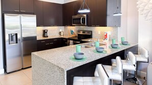 Une cuisine moderne avec des meubles de couleur sombre, des appareils en acier inoxydable, un comptoir en granit et un coin bar agrémenté de tabourets blancs.
