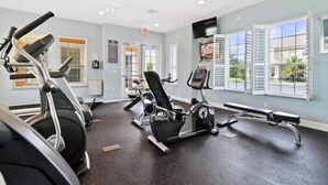 Une salle de sport équipée de machines de cardio, d’un banc et de fenêtres avec des stores.