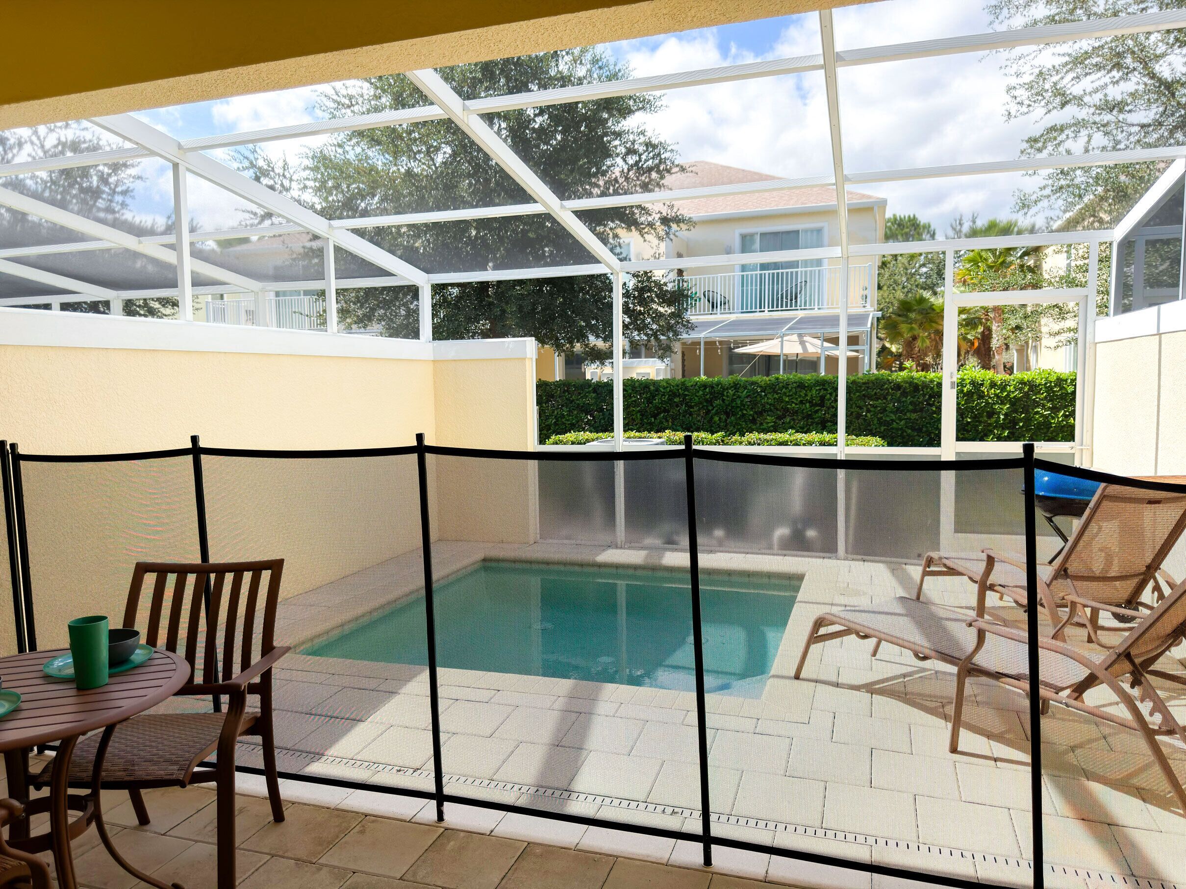 A covered outdoor pool area with a table and chairs, surrounded by a white fence.