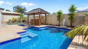 Un patio trasero con piscina, un quiosco de madera y un área cercada con palmeras.