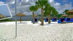 A beach with a volleyball net, palm trees, and beach chairs under thatched umbrellas. - BB614NPP - Relaxing 3BR Corner Condo • Sleeps 6 (Davenport)