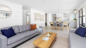 A modern living room with a grey sofa, a wooden coffee table, and a dining area with grey chairs. - Jindee Beach 2km away | Magical memories in Butler (Butler)