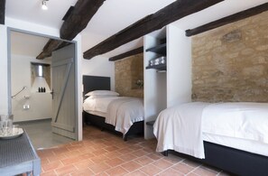 Une chambre avec deux lits, un mur en pierre et une porte donnant sur une autre pièce.