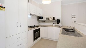 Une cuisine de taille réduite avec des meubles blancs, une cuisinière, un four, un four à micro-ondes et un évier.