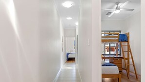 Un couloir étroit, avec un lit superposé et un bureau sur le côté droit, qui mène à une chambre comprenant un lit et une fenêtre.