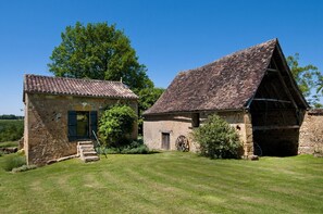 A stone building with a tiled roof, a wooden door, and a wheel in the foreground.