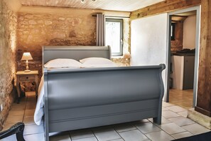 A bedroom with a bed, a nightstand, a lamp, a stone wall, and a window.