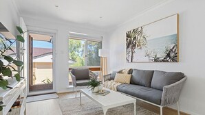 A modern living room with a grey sofa, a white coffee table, and a large window offering a view of the outdoors. - Bright & Stylish by the Sea! (Scarborough)