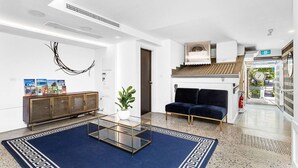 A modern lobby with a glass coffee table, a dark blue sofa, a wooden cabinet with magazines, and a potted plant. - Stylish & Comfortable 1-Bedroom Hotel Room with Rooftop Access (Perth)