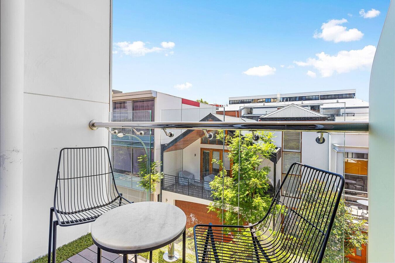 A balcony with two chairs and a table, overlooking a cityscape with buildings and a clear sky.