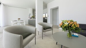 Una sala de estar moderna con un sofá, sillones y una mesa de centro. Hay un jarrón con flores sobre la mesa.