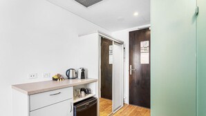 A compact kitchenette with a countertop, a coffee maker, a kettle, and a dishwasher.