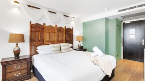 A neatly made bed with white linens, two bedside tables with lamps, a wooden headboard, and a green accent wall. - Nest on Newcastle – E4 (Perth)
