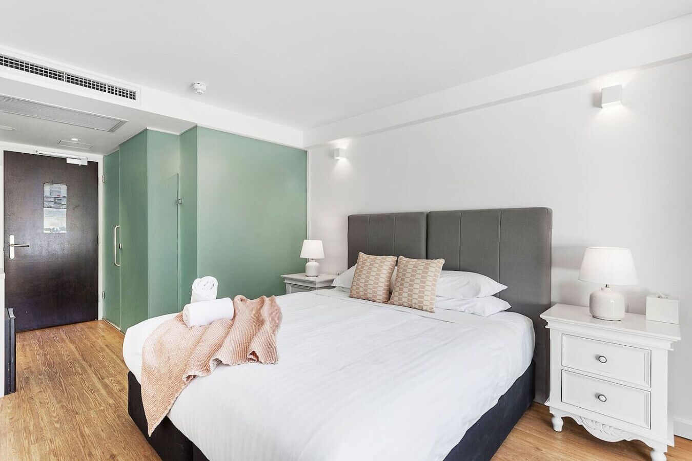 A modern hotel room with a large bed, two bedside tables with lamps, a wardrobe, and a door with a view.