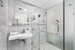 A modern bathroom with a glass shower enclosure, a sink with a mirror, and a "PULL" sign on the shower door.