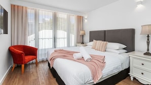 A hotel room with a bed, a red chair, a nightstand, and a lamp.