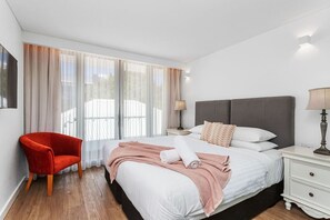 A hotel room with a bed, a red chair, a nightstand, and a lamp. - Nest on Newcastle – E6 (Perth)