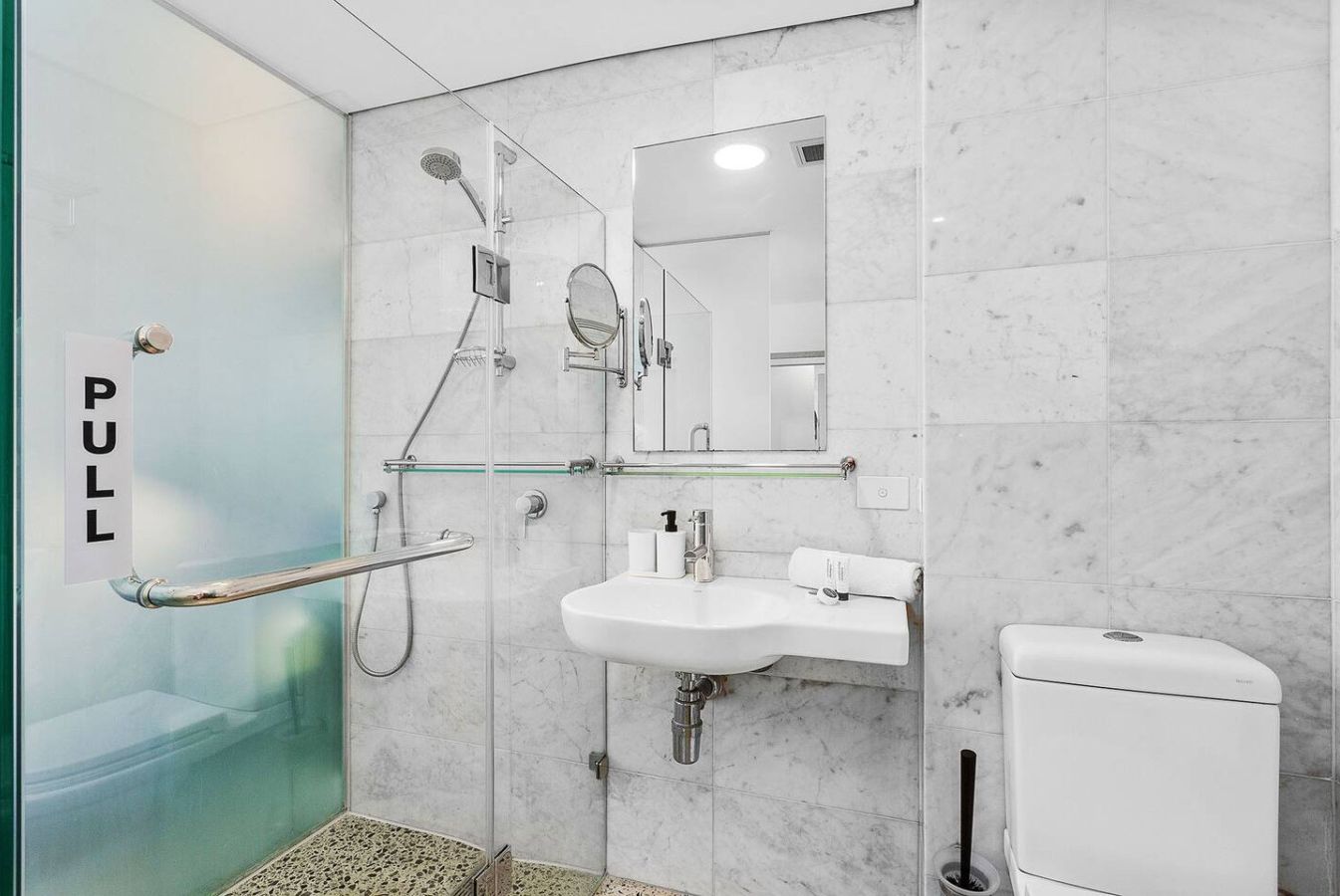 Ein modernes Badezimmer mit Duschkabine aus Glas, einem weißen Waschbecken, einem Spiegel und einer Toilette.