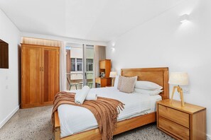 Un dormitorio con una cama de madera, mesitas de noche, un armario y un escritorio con una silla.