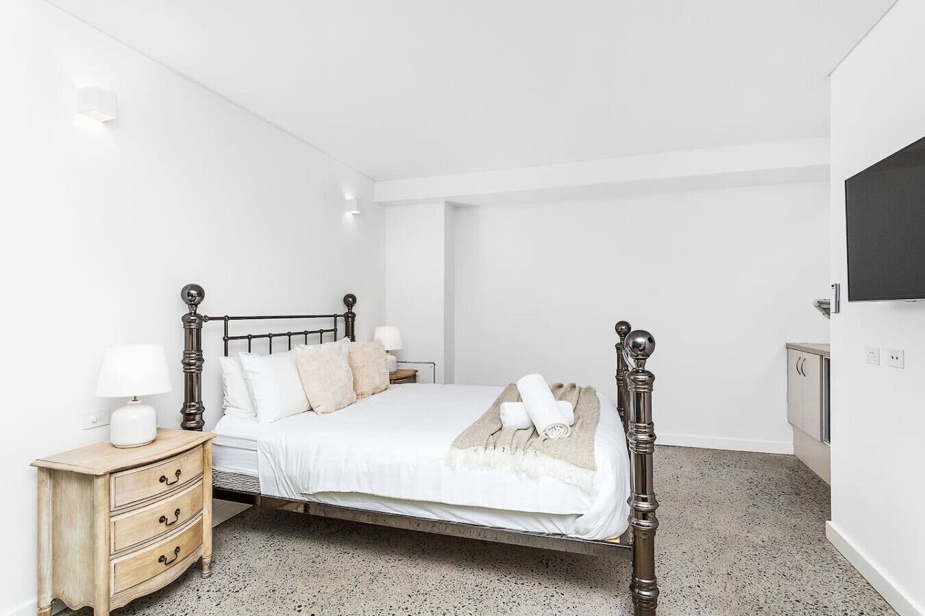 A bedroom with a bed, bedside tables, a dresser, and a TV mounted on the wall.