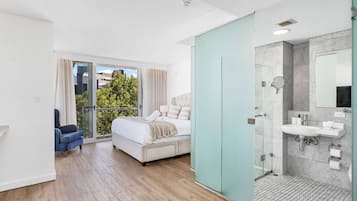 A modern bedroom with a large bed, a balcony with a view, and a separate bathroom with a shower and sink.