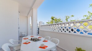 Een witte tafel met stoelen en oranje servetten, een wit hek en een bloempot.