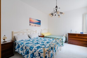 Ein Schlafzimmer mit Bett, Nachttisch, Kommode, einer Chandelierleuchtre und einem Wandbild.