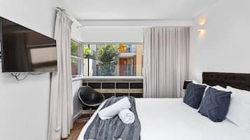 A hotel room with a bed, a TV mounted on the wall, a chair, and a window with curtains.