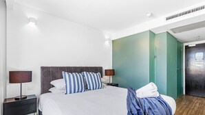Quarto de hotel moderno com uma cama grande, duas mesas de cabeceira com luminárias, uma parede de destaque verde e piso de madeira.