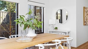 A modern dining area with a wooden table, white chairs, a potted plant, and a round mirror on the wall. - Spacious & modern Dianella! (Dianella)