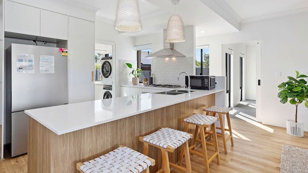 A modern kitchen with a central island, bar stools, pendant lights, and a view of the outdoors. - Spacious & modern Dianella! (Dianella)
