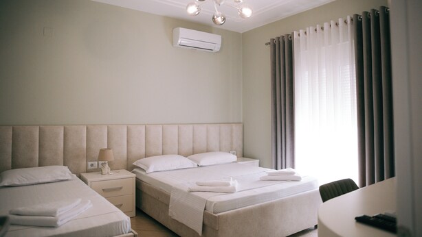 A hotel room with a large bed, a smaller bed, a bedside table with a lamp, a chair, and a desk. - Vila Merkaj (Berat)