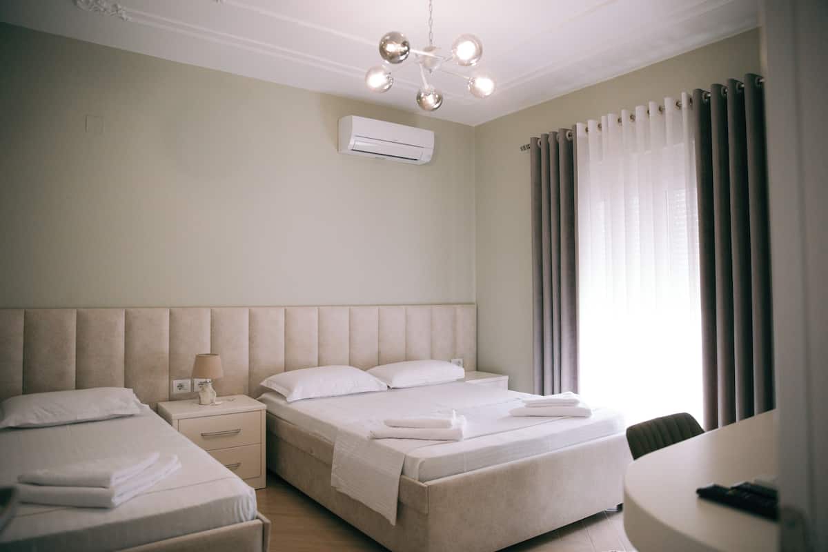 Habitación de hotel con una cama grande, una cama más pequeña, una mesita de noche con lámpara, una silla y un escritorio.