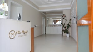 A reception area with a wooden reception desk, a potted orchid, and a view into the hallway leading to a kitchen area. - Vila Merkaj (Berat)