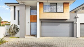 Een modern herenhuis met garage, klein portaal en oprit van baksteen.