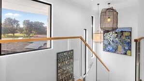 Een modern interieur met uitzicht op een park door een groot raam, een houten trap, een wandlamp en een schilderij met cactussen.
