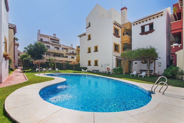 A swimming pool surrounded by buildings with balconies and a clear sky.
