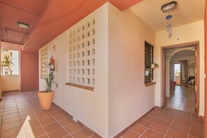Un couloir avec un sol carrelé, une plante en pot, un mur blanc orné d’un motif quadrillé et une porte donnant sur une autre pièce.