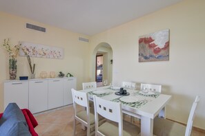 Un coin repas avec une table blanche dressée pour quatre personnes, des chaises blanches, un meuble blanc agrémenté d’objets décoratifs et un tableau accroché au mur.