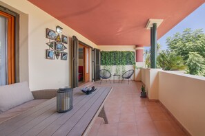 A balcony with a wooden table, two chairs, a potted plant, and a wall adorned with framed pictures and a green plant wall.