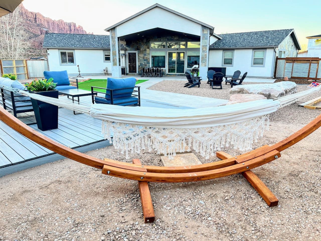 Un hamac avec une structure en bois, un espace patio aménagé avec du mobilier d’extérieur et une maison à la façade en pierre.