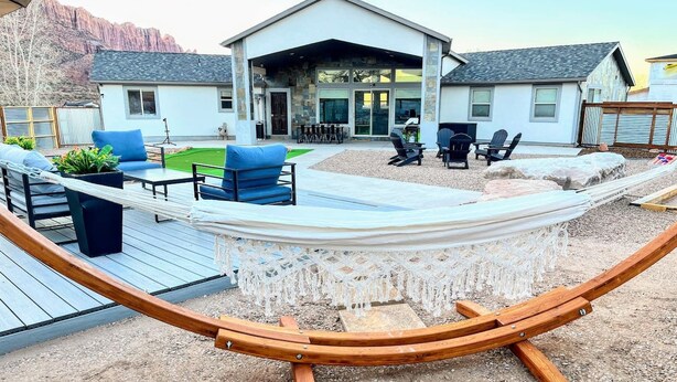 A hammock with a wooden frame, a patio area with outdoor furniture, and a house with a stone facade. - MtnViews–Hot tub-Mini Golf–Bocce–Pool Table–3000sf (Moab)