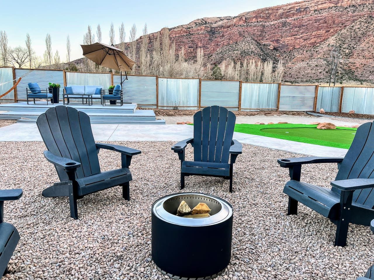 Un espace patio aménagé avec des fauteuils Adirondack, un foyer et une vue sur une pelouse verdoyante et des montagnes en arrière-plan.